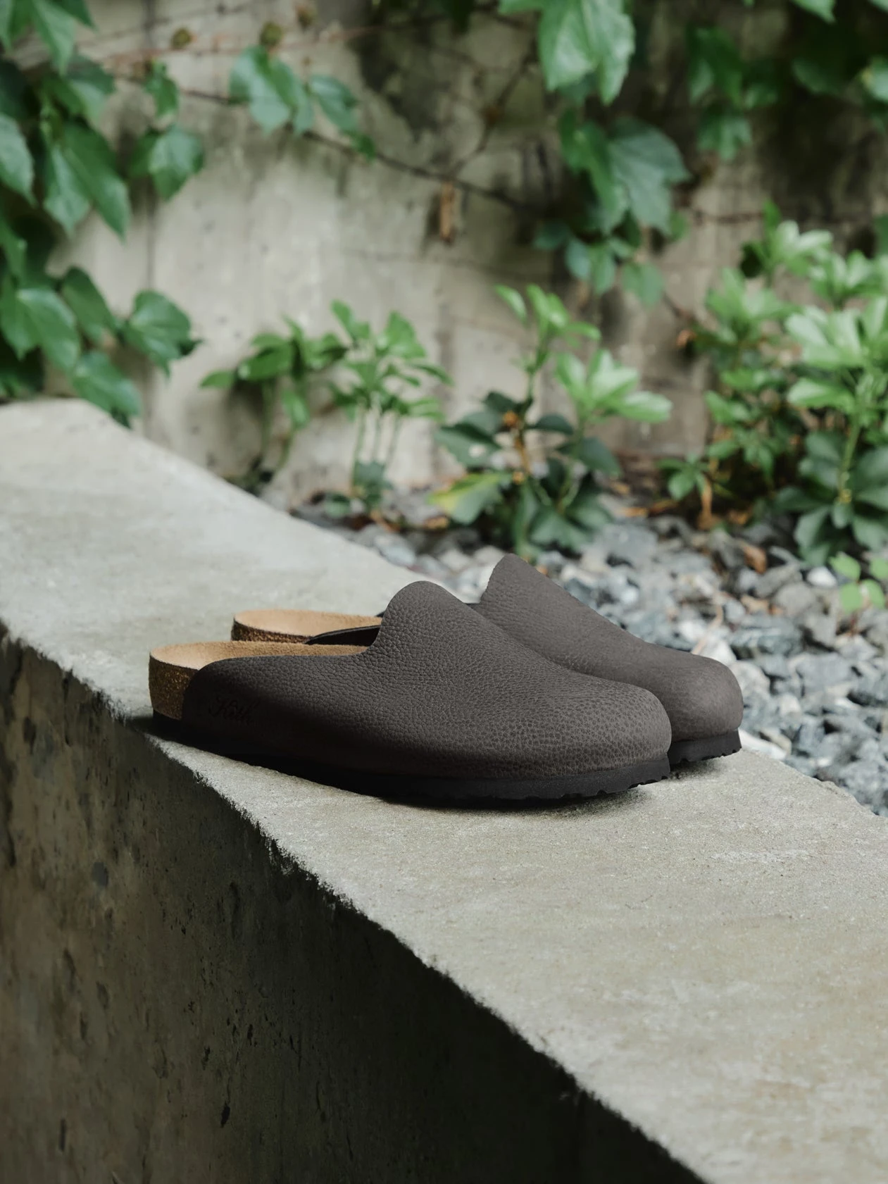 A black suede Amsterdam clog pair on a bare concrete ledge